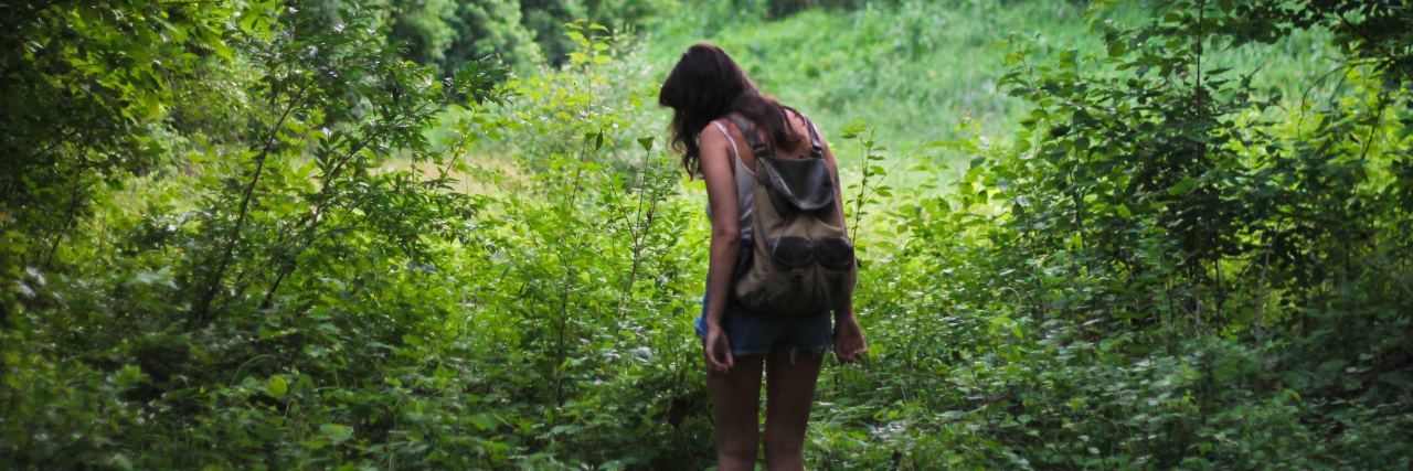 back of woman in t shirt and shorts with a backpack on exploring in a forest