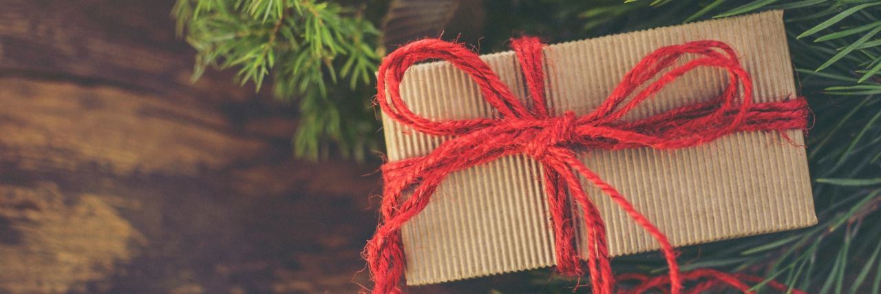 brown paper package wrapped with a red string sitting on a wooden table with pine branches surrounding