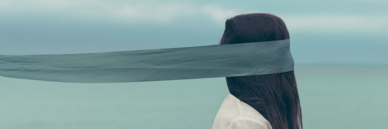 How I Manage Having Disturbing Thoughts Due to Schizophrenia woman next to sea with fabric covering face and eyes