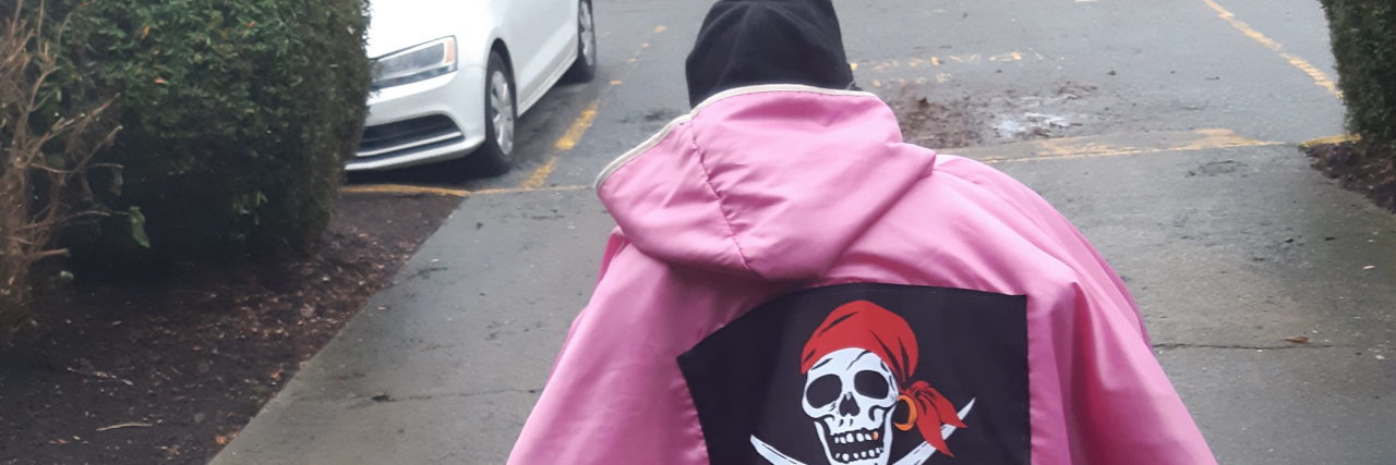 Jennifer in her wheelchair wearing a bright pink coat with a pirate patch on the back.