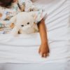 Child in bed hugging a teddy bear.