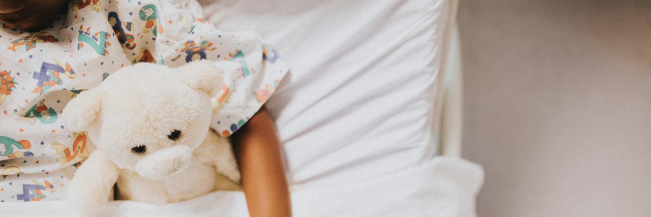 Raising a Daughter With Turner Syndrome Child in bed hugging a teddy bear.