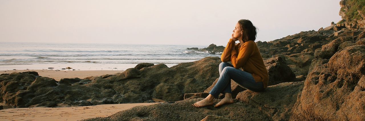 What You Need to Know About Eating Disorder Recovery photo of woman sitting on beach with chin resting on hand, looking out to sea