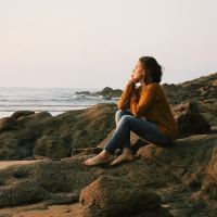 photo of woman sitting on beach with chin resting on hand, looking out to sea
