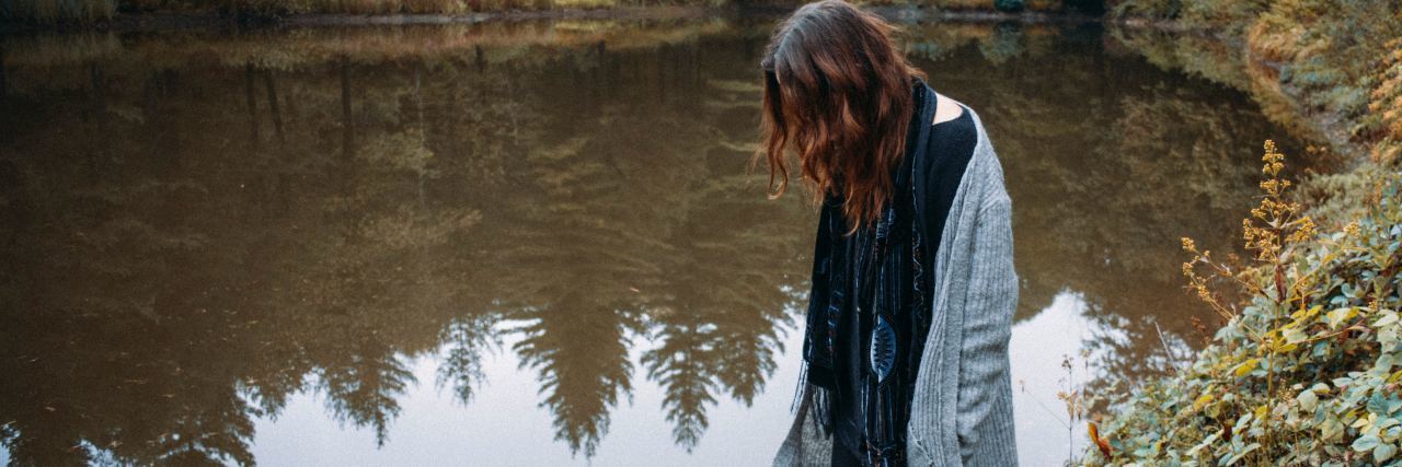 What Life and Healing Is Like With Lyme Disease photo of woman standing in forest by lake or pond and looking into the water, her hair hiding her face