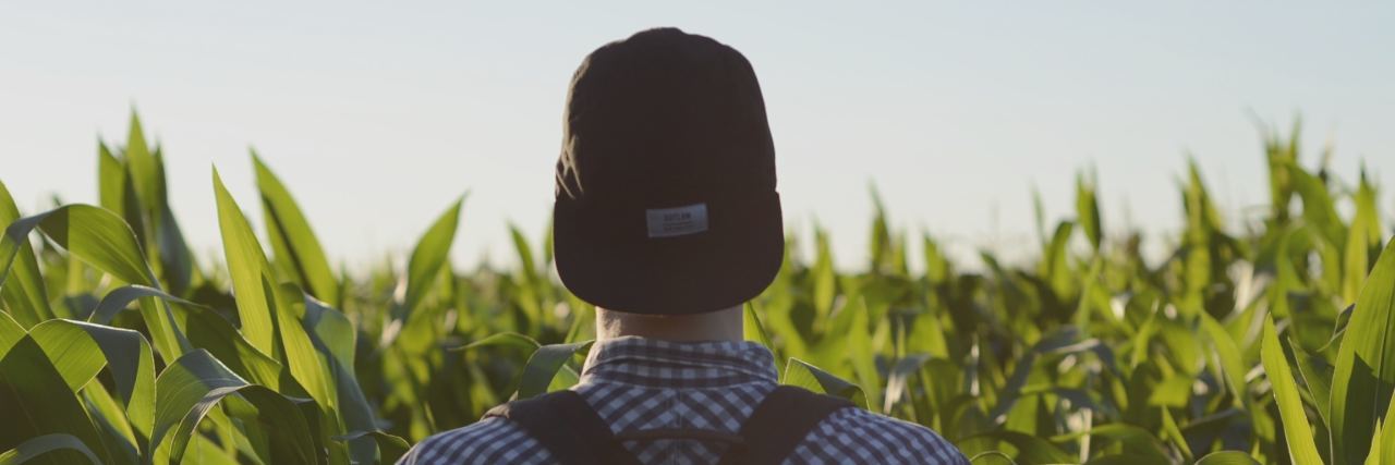 Don't Let What You Think Others Will Think Control Your Mental Health back of man in a collared sheet with a black hat on backward standing in a field