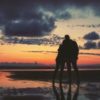 photo of couple standing close silhouetted by sunset on beach