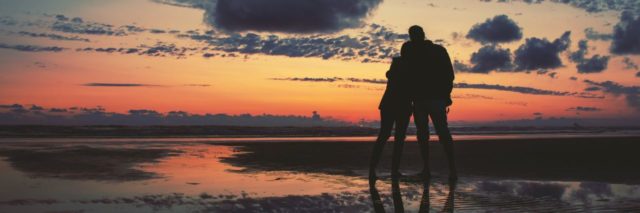 photo of couple standing close silhouetted by sunset on beach