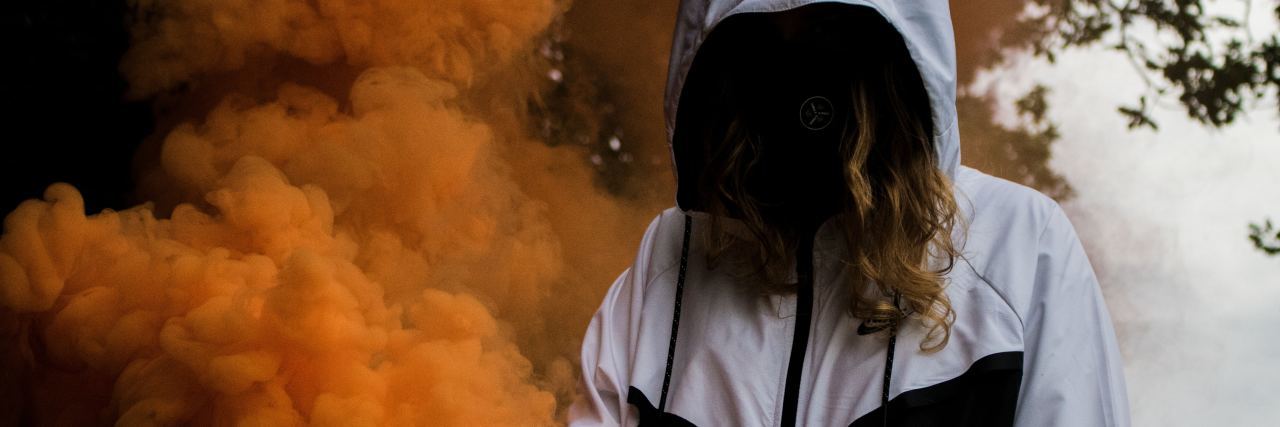 Having a Complex PTSD 'Hangover' After Being Triggered photo of woman with face covered by dark hair and hooded jacket, surrounded by orange smoke