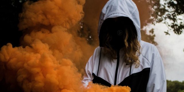What It’s Like to Have a Complex PTSD 'Hangover' photo of woman with face covered by dark hair and hooded jacket, surrounded by orange smoke