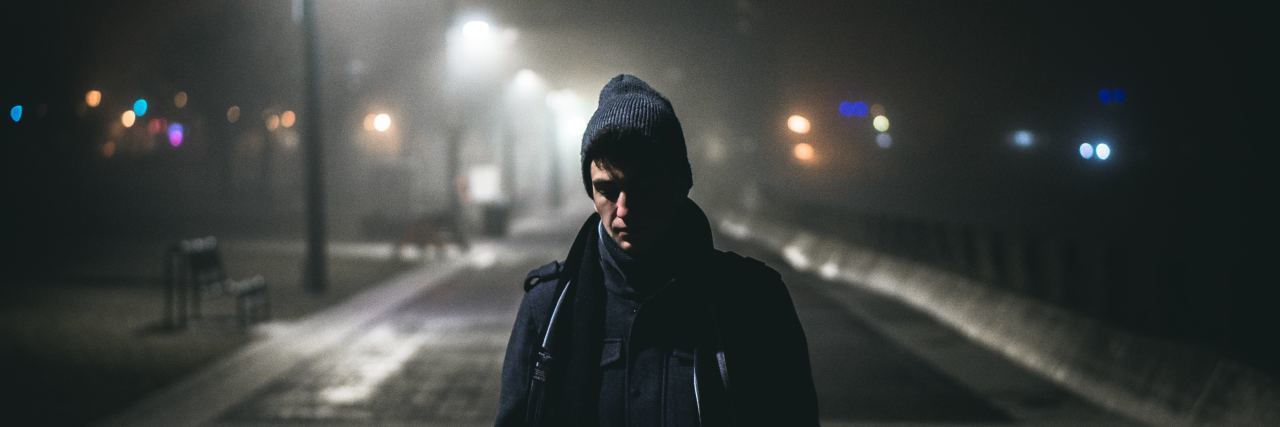 man in a beanie and blue jacket walking with his head down on a dark, cold sreet