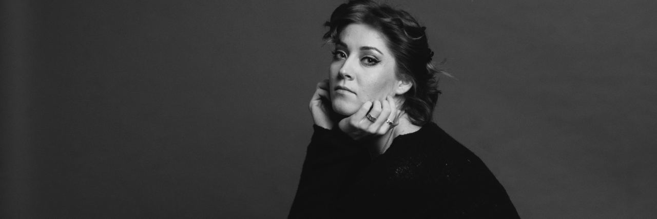 Losing My Trauma Therapist Taught Me I Am Loved black and white photo of woman sitting on stool looking sad at camera with chin resting on hands
