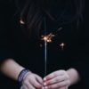 close up photo of woman holding sparkler against dark clothing