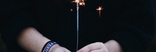 close up photo of woman holding sparkler against dark clothing