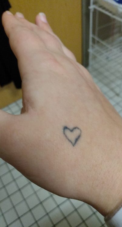 Mae shows the viewer a tattoo of a heart, which is located on her hand.