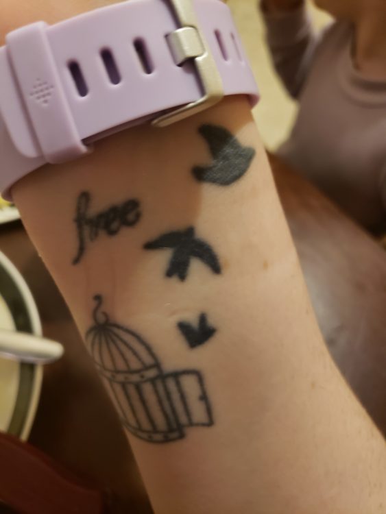 Angelica shows the viewer a tattoo of three birds that are flying out of the cage. They are supposed to represent the same bird flying more and more steadily as it gets farther away from the cage. The word 'free' is written in cursive.