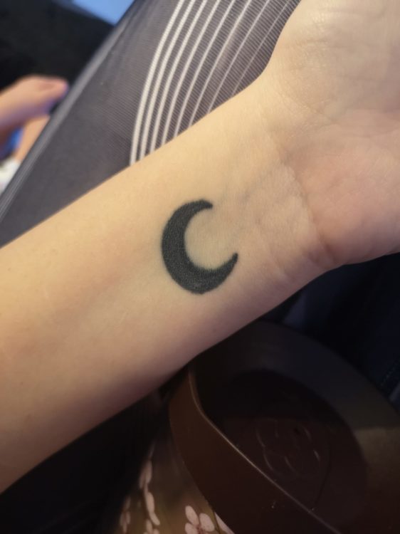 Madeline shows the viewer the crescen moon tattooed on her arm.