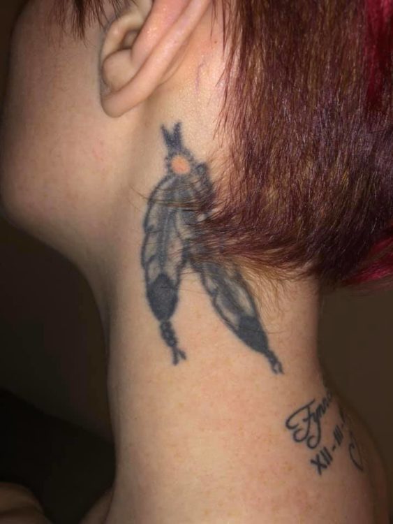 A woman who used to have BD shows off a neck tattoo of two feathers held together by a red bead. The feathers are white with black tips and appear just below the woman's ear.