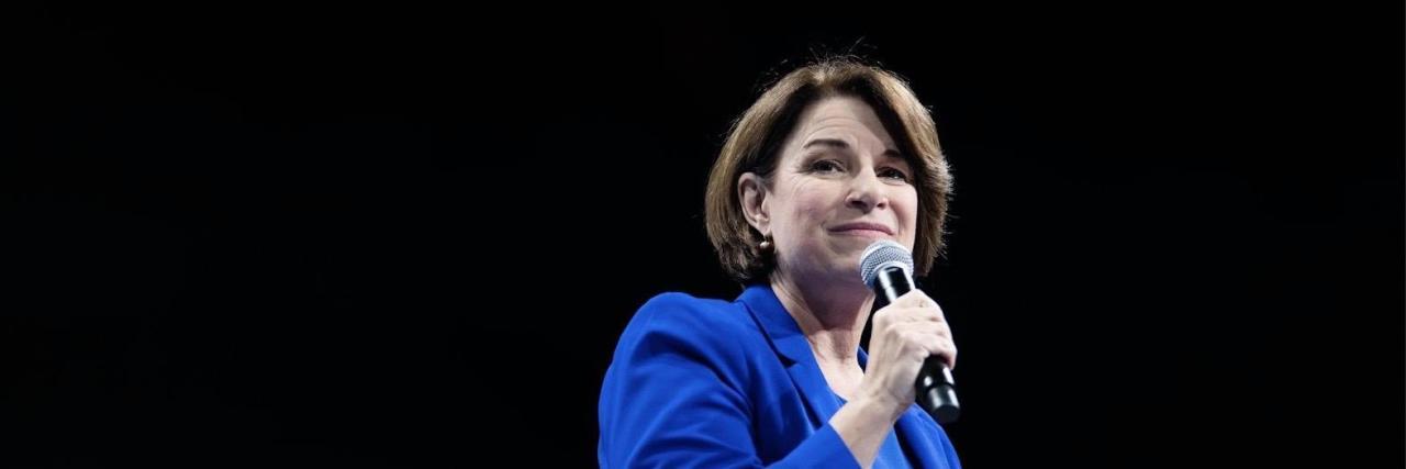 Amy Klobuchar wearing a blue suit, holding a microphone.