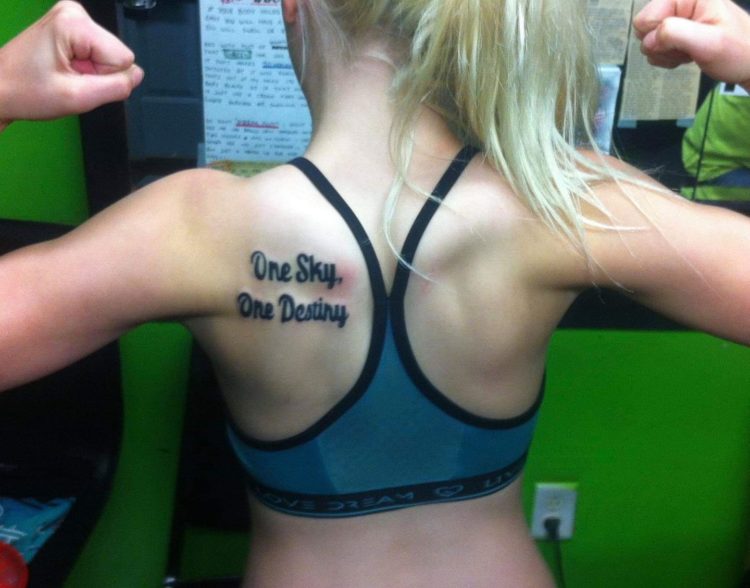 Keara shows off a tattoo on her back. It reads, 'One Sky, One Destiny.' She is flexing her arms.