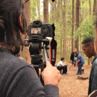 Filmmaker looking through a camera at scene in the woods