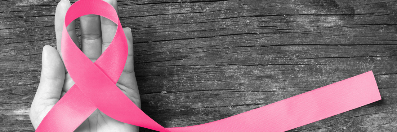 5 Things I Wish I Knew Before My Bilateral Mastectomy A pink ribbon, the symbol for breast cancer awareness, is wrapped above the palm of a person's hand. Only the pink of the breast cancer awareness ribbon has color; the rest of the image is somber grey.