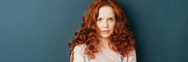 woman with curly red hair standing with arms folded staring at camera
