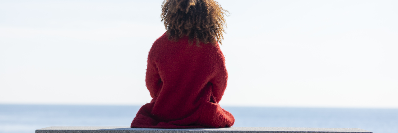 Dealing With Grief and Learning to Accept Yourself With Fibromyalgia focus on the back of a woman sitting on a bench in front of the water
