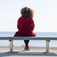 focus on the back of a woman sitting on a bench in front of the water