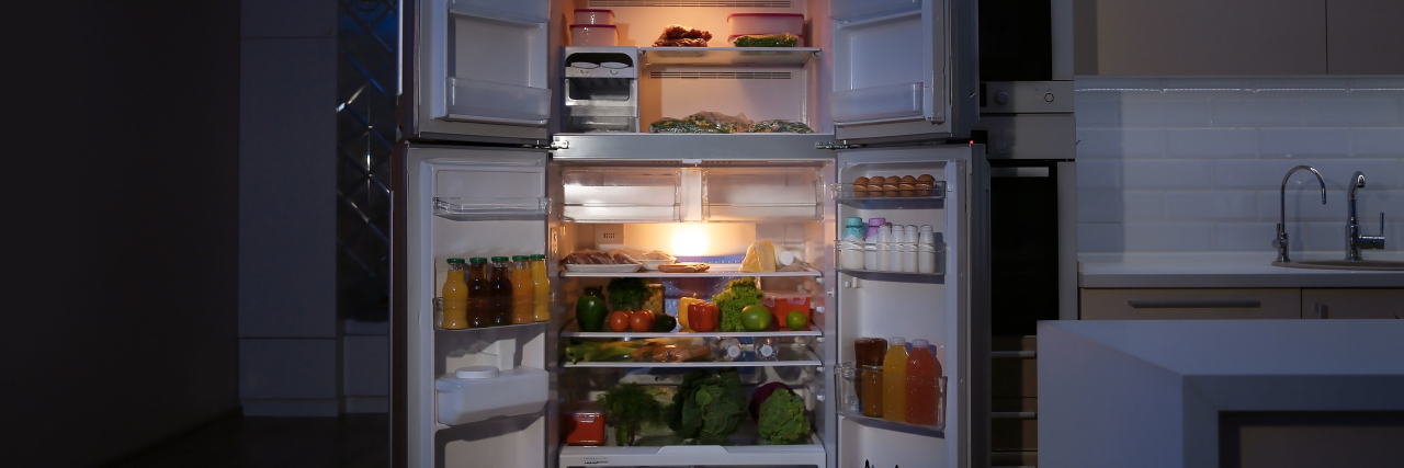 What Hunger Actually Feels Like With Prader-Willi Syndrome Open refrigerator filled with food in kitchen at night