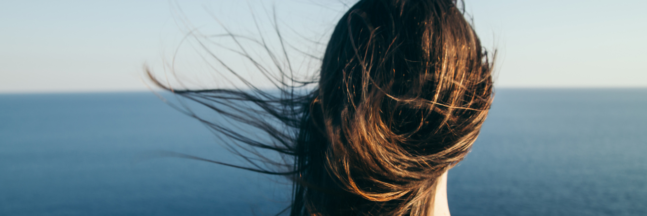 Changing As a Person After Chronic Illness Diagnosis Woman with dark hair stands on a top cliff over blue sea