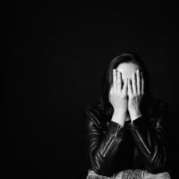 Portrait of a woman in a leather jacket with her hands over her face