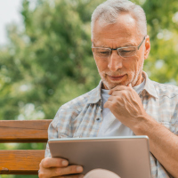 Man sitting outside on park bench thoughtfully looking at a tablet