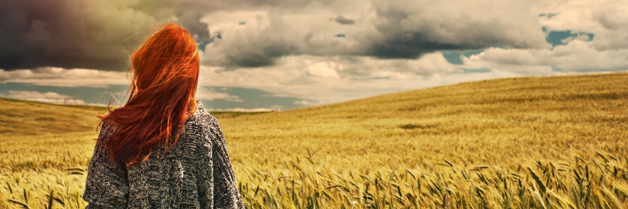 Tips for Dealing With a Progressive Illness young woman standing in a wheat field, facing the sky and clouds
