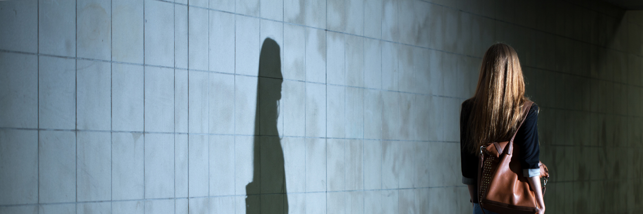 Woman walking, her shadow cast on the wall.