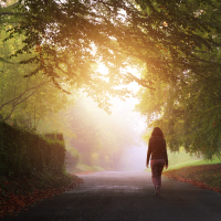 A woman walks towards the light on a misty day on a country road.