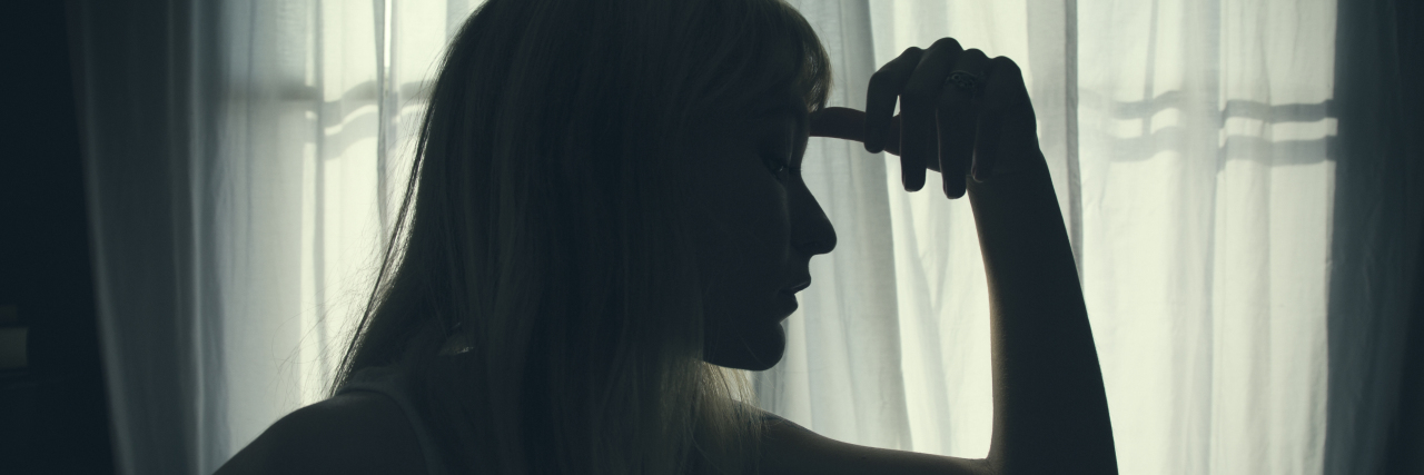 The Medical Trauma I Experience From Congenital Heart Disease silhouette of a woman sitting in bed by a window thinking