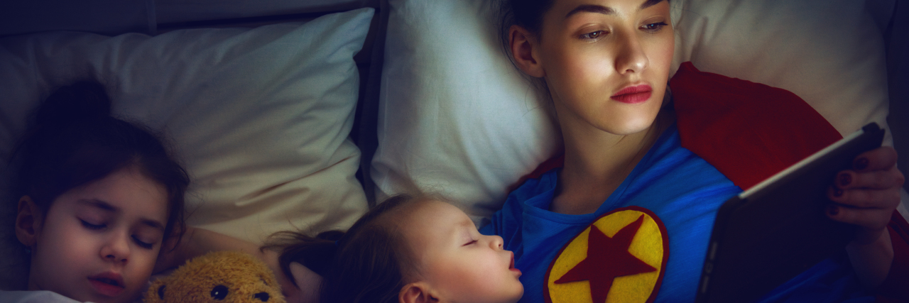 3 Helpful Tips for When You're Feeling Like a Burned Out Mama a mom wearing a superhero shirt laying in bad with her sleeping children