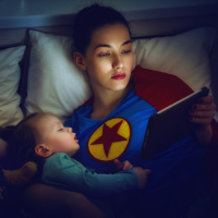 a mom wearing a superhero shirt laying in bad with her sleeping children