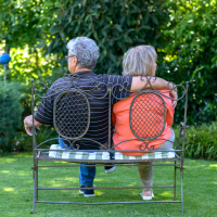 an older couple sitting on a bench in a green garden