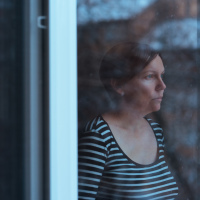 woman with short red hair in a striped shirt looking out the window solemnly