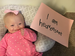 A babygirl with Down syndrome laying in a boppy with a sign that says "I am heavensent."