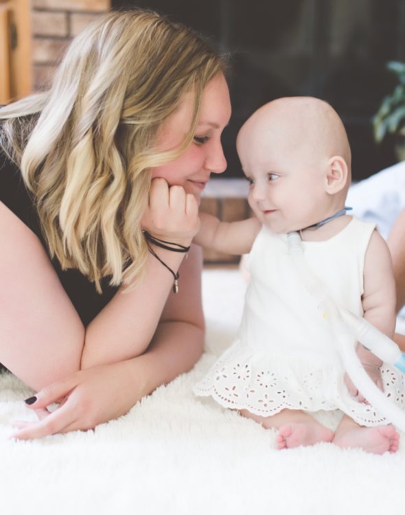 a mother smiling at her infant daughter and holding her hand