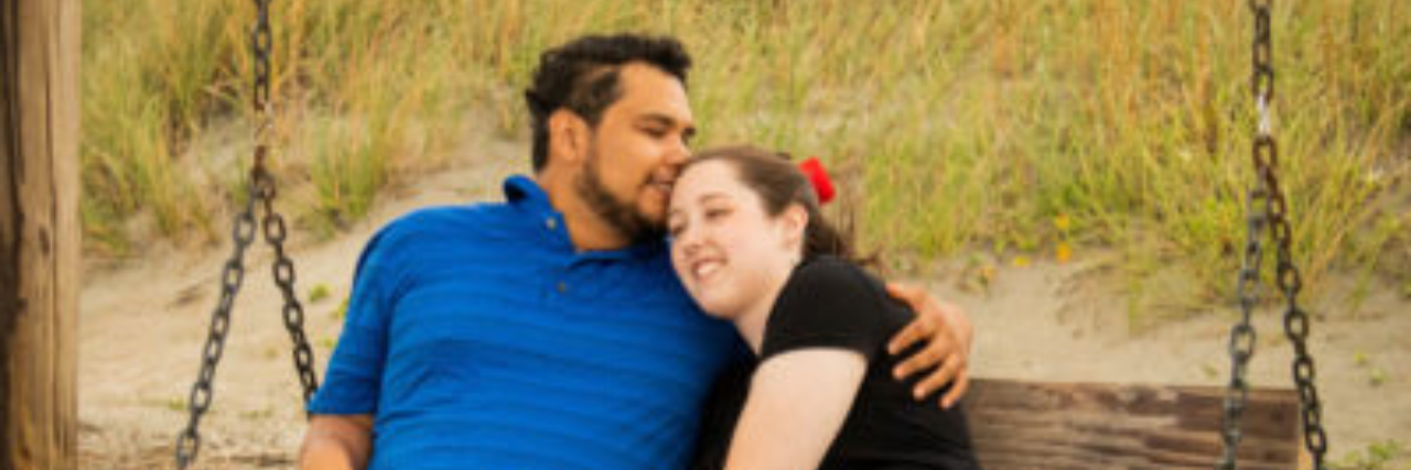 Therapist Helped Me Figure Out How to Disclose Illness to My Partner photo of author and husband sitting on a bench, husband kissing her forehead
