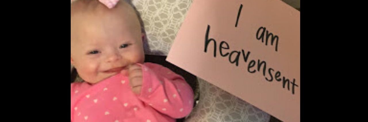 What to Say (and Not Say) to Parents of a Child With Down Syndrome A babygirl with Down syndrome laying in a boppy with a sign that says "I am heavensent."