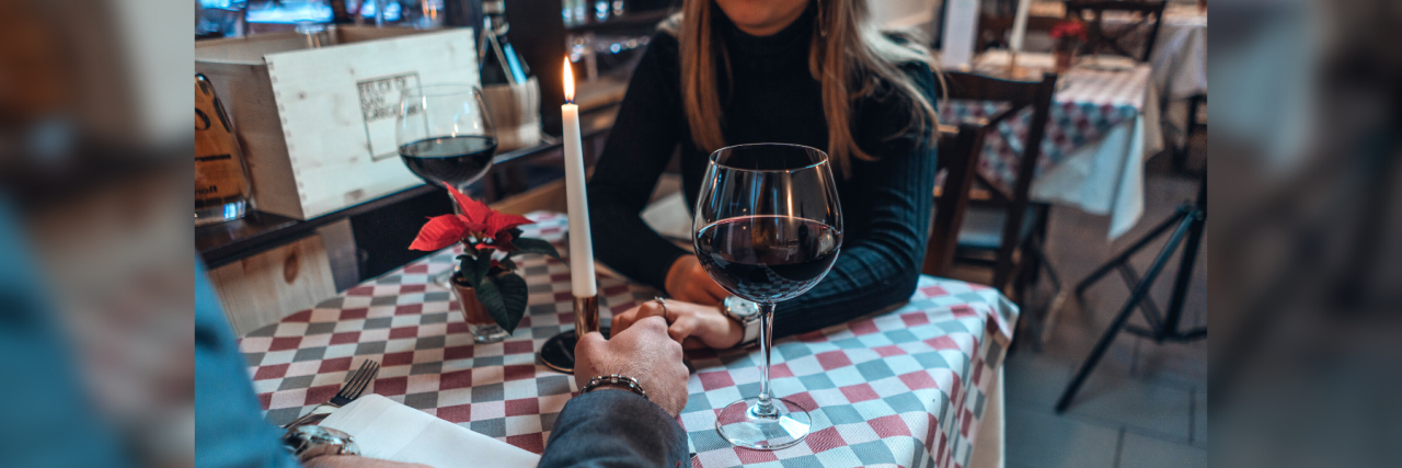 When Should You Reveal Your Mental Illness in a New Relationship? photo of couple in restaurant with hands meeting across table, a candle between them