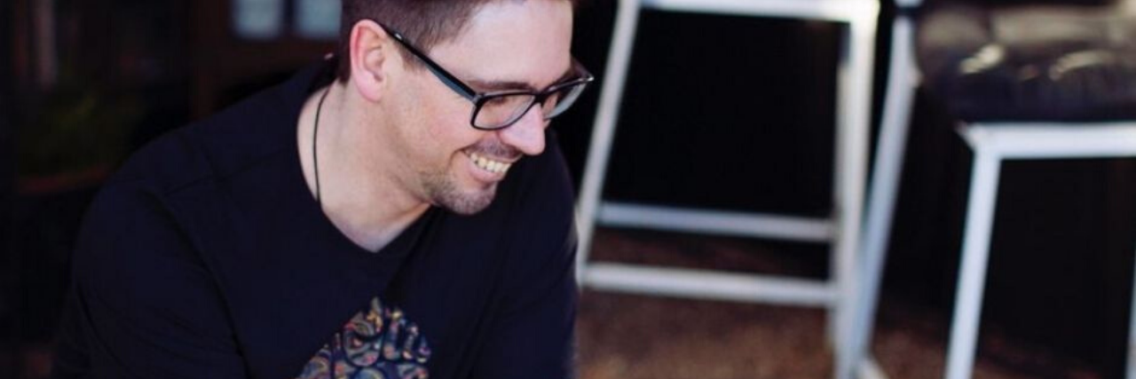 Taking a Risk and Changing Career to Help Mental Health photo of man wearing glasses and with arm tattoos sitting at table in cafe with coffee cup