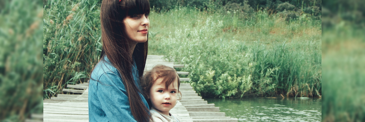 photo of young mother with dark hair sitting on pier with young child on her lap