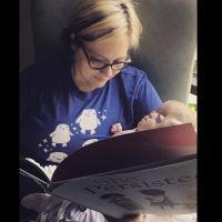 A mother cradling her baby and reading a book in the NICU.