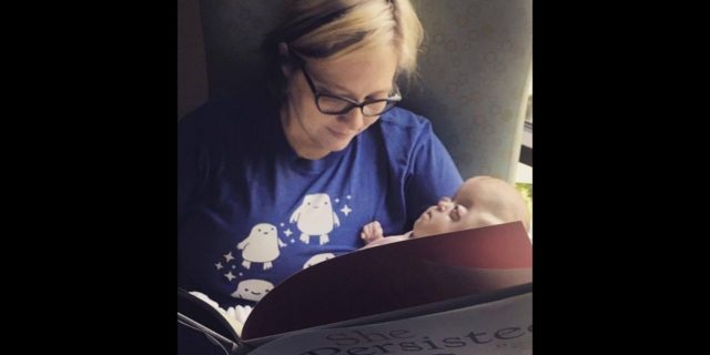 A mother cradling her baby and reading a book in the NICU.